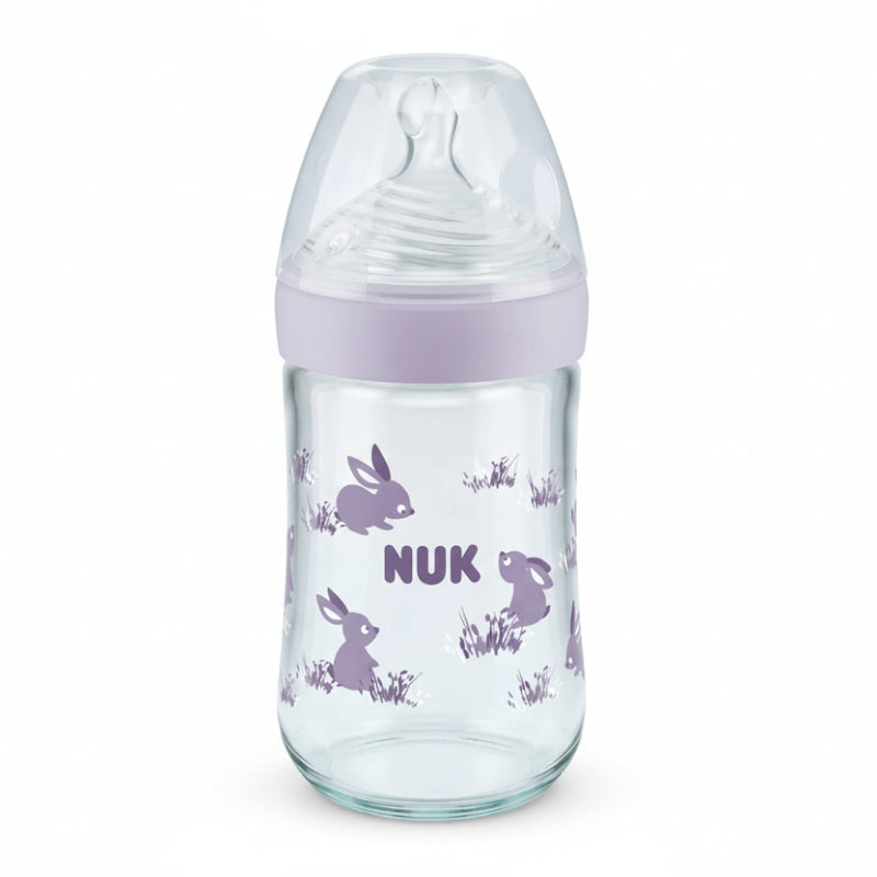 Glass baby bottle with purple cap and rabbit illustrations on a white background, featuring the NUK brand.